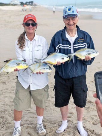 Happy couple show off their pompano reward after surf fishing with Cocoa Beach Surf Fishing Charters.