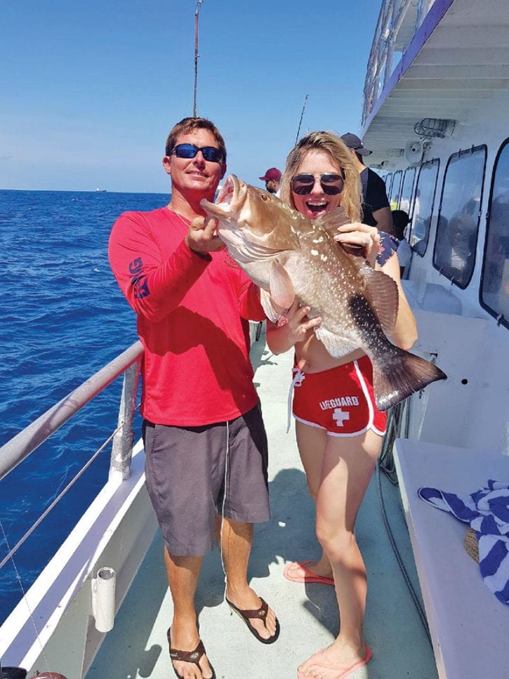 Capt Rod helps guest show off her big red grouper caught aboard the Catch My Drift.