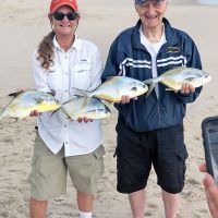 Happy couple show off their pompano reward after surf fishing with Cocoa Beach Surf Fishing Charters.