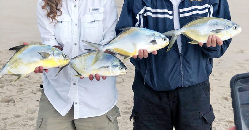 Happy couple show off their pompano reward after surf fishing with Cocoa Beach Surf Fishing Charters.