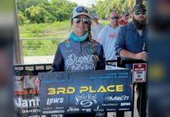 Wendy Biles in a cap, sunglasses and a tournament jersey holding a 3rd Place banner from the September 7, 2024 kayak bass tournament on Lake Toho, with other anglers behind her
