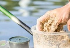 Hands mixing homemade chum in a clear plastic tub beside the water, next to a small bait container