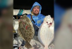 Capt. John Ellis in a blue Reef Wrecker hoodie holding up two big flounder on his boat at night, one dark side up and one white side up