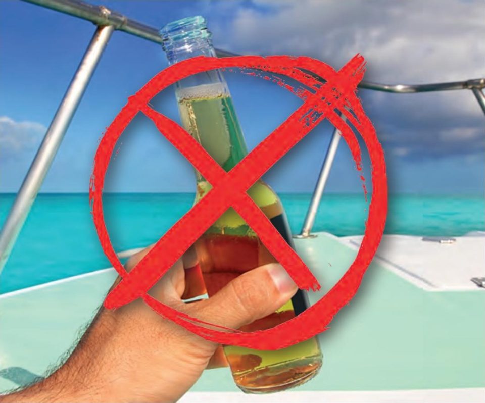 A hand holding a glass beer bottle on a boat with turquoise water behind it, crossed out with a red circle and X
