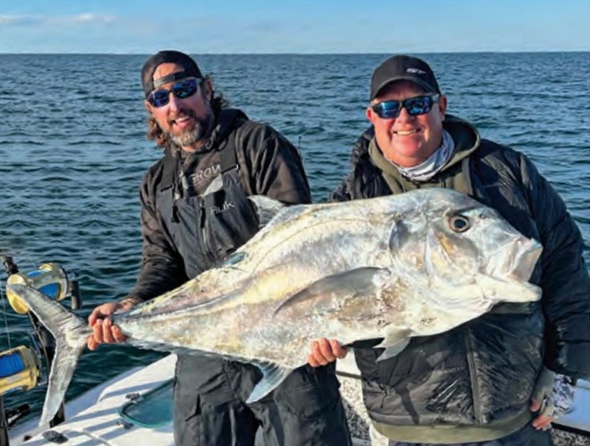Two anglers in caps and sunglasses holding up a huge African pompano on a boat, with the open Atlantic behind them