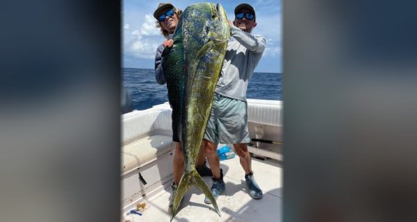 Brothers Austin and Cole Ferguson in caps and blue mirrored sunglasses holding up a huge mahi between them on the deck of a boat offshore