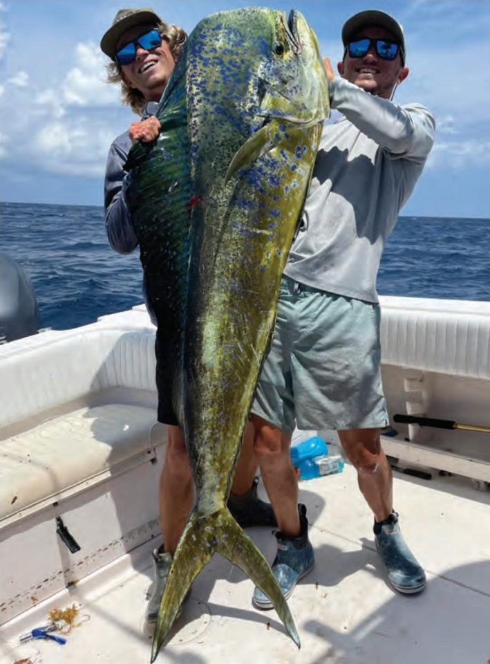 Brothers Austin and Cole Ferguson in caps and blue mirrored sunglasses holding up a huge mahi between them on the deck of a boat offshore