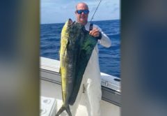 Capt. Scott Housel in sunglasses holding up a big mahi on his boat offshore, with blue water behind him