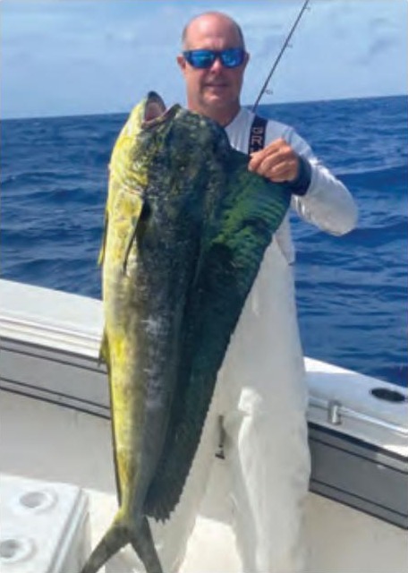 Capt. Scott Housel in sunglasses holding up a big mahi on his boat offshore, with blue water behind him