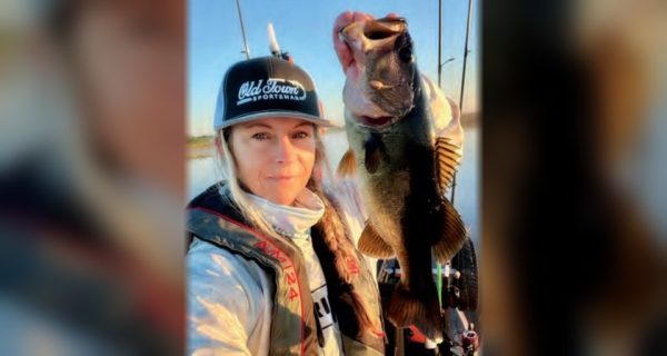 Wendy Biles in an Old Town Sportsman cap and life vest holding up a largemouth bass by the lip