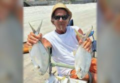 Marco Pompano holding up a pompano in each hand on the beach, with more pompano piled on a cooler in front of him