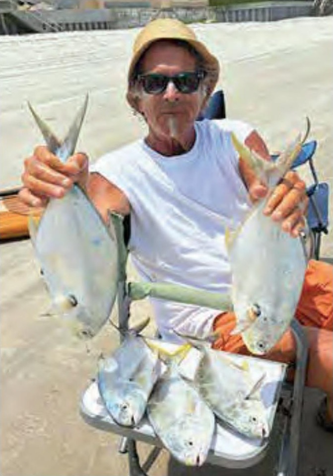 Marco Pompano holding up a pompano in each hand on the beach, with more pompano piled on a cooler in front of him