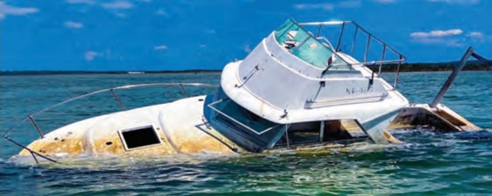 A half sunken derelict cabin cruiser listing in green water under a blue sky