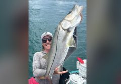 An angler in a white cap and sunglasses holding up a big snook in his kayak