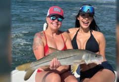 Two smiling anglers in sunglasses holding a snook together on a boat