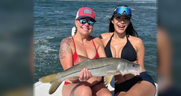 Two smiling anglers in sunglasses holding a snook together on a boat