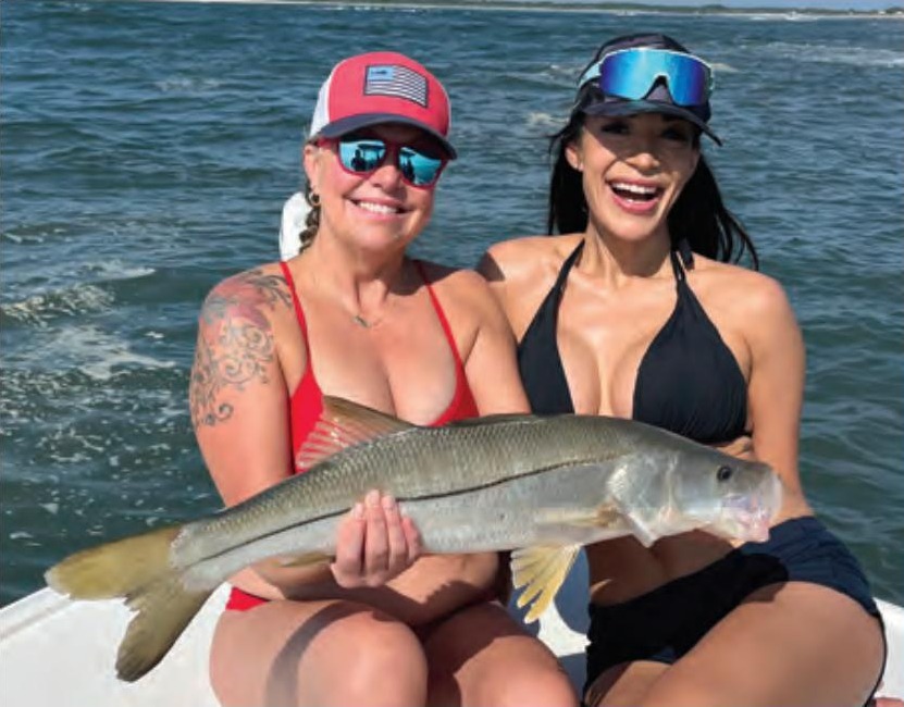 Two smiling anglers in sunglasses holding a snook together on a boat