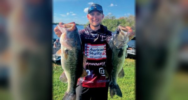 Pro bass angler Joey Bloom holding up two big largemouth bass on a lakeshore