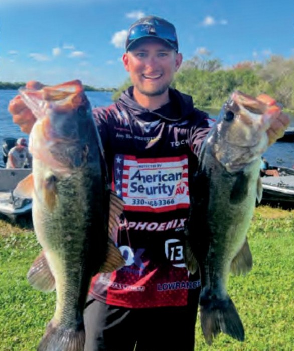 Pro bass angler Joey Bloom holding up two big largemouth bass on a lakeshore