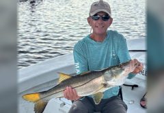 An angler in a cap and sunglasses holding a big snook on a boat