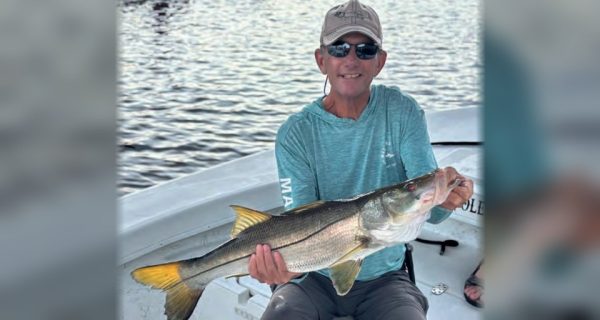 An angler in a cap and sunglasses holding a big snook on a boat