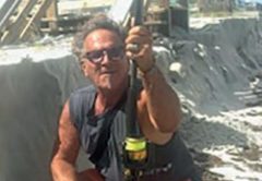 Marco Pompano crouching with a surf rod below a sand cliff cut into the beach at Wilbur by the Sea, with a damaged beach walkover behind him