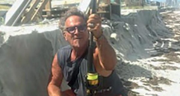 Marco Pompano crouching with a surf rod below a sand cliff cut into the beach at Wilbur by the Sea, with a damaged beach walkover behind him
