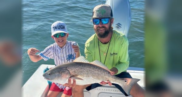 Capt. Jeff Patterson of Pole Dancer Fishin' Charters and a young angler holding a redfish on his boat