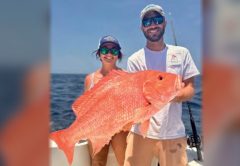 A woman and a man holding a large red snapper on a boat offshore