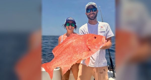 A woman and a man holding a large red snapper on a boat offshore