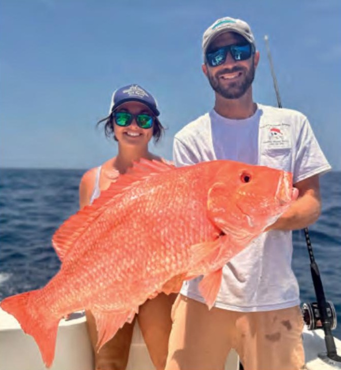 A woman and a man holding a large red snapper on a boat offshore