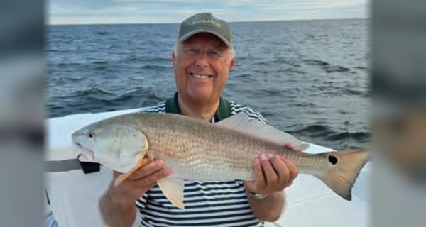 An angler in a cap and striped shirt holding a redfish on a boat