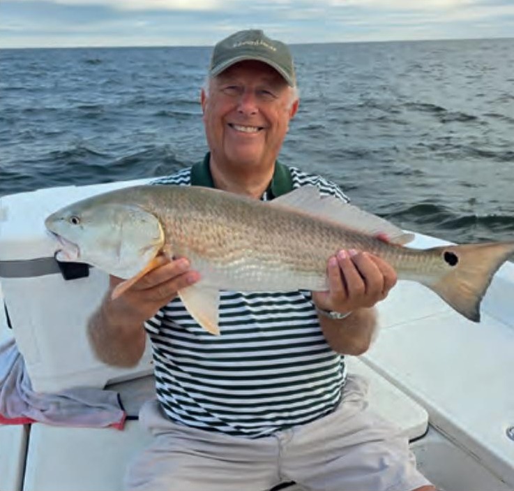 An angler in a cap and striped shirt holding a redfish on a boat