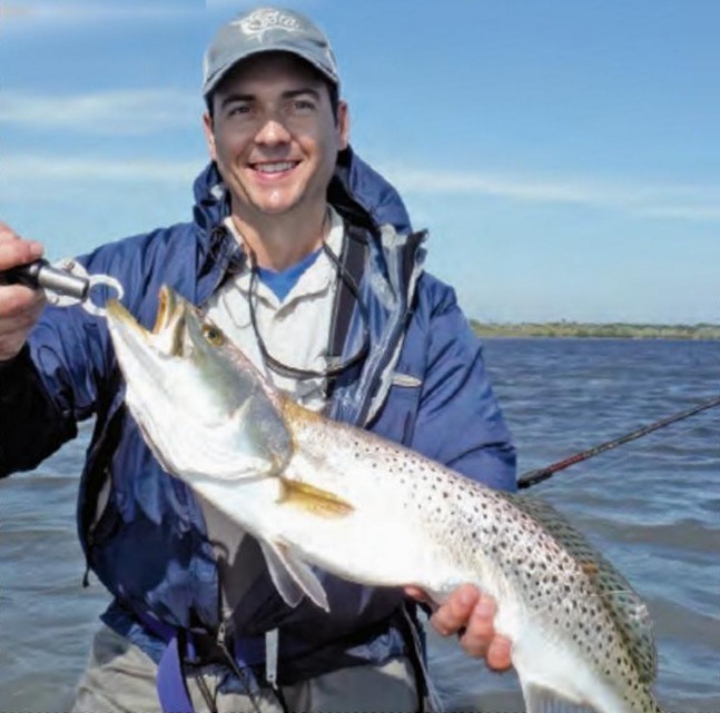 An angler in a blue jacket holding a big speckled trout