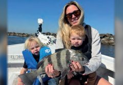 A woman and two young children holding a sheepshead on a boat near the jetty rocks