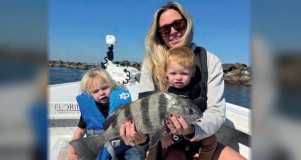 A woman and two young children holding a sheepshead on a boat near the jetty rocks