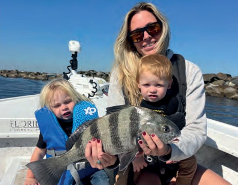 A woman and two young children holding a sheepshead on a boat near the jetty rocks