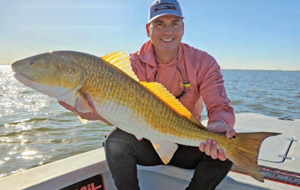 An angler kneeling on a boat deck holding a big redfish