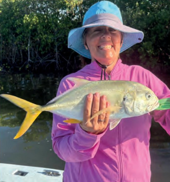 An angler in a blue sun hat holding a jack crevalle in front of the mangroves