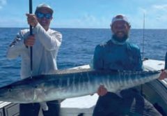 Two anglers holding a big wahoo on a boat offshore