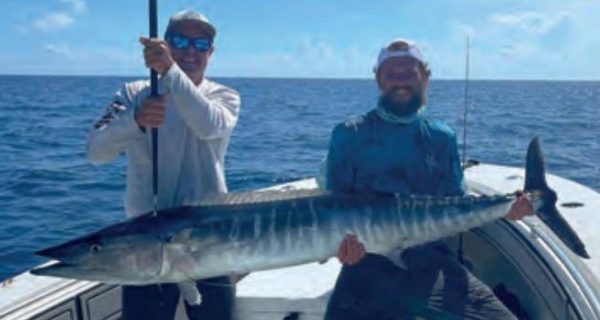 Two anglers holding a big wahoo on a boat offshore