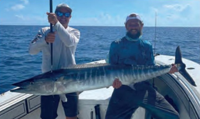 Two anglers holding a big wahoo on a boat offshore
