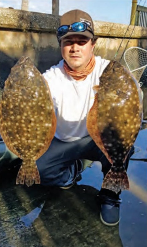An angler crouching with a flounder in each hand