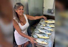 A smiling woman beside a cleaning table full of freshly caught pompano