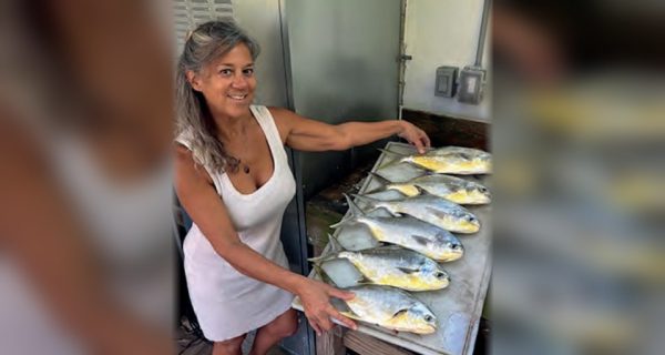 A smiling woman beside a cleaning table full of freshly caught pompano