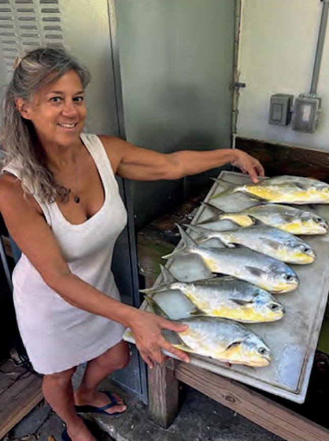 A smiling woman beside a cleaning table full of freshly caught pompano