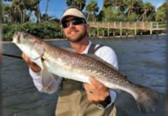 A wading angler in a visor and sunglasses holding a big speckled trout