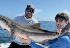 Two anglers holding a big cobia on the deck of a boat