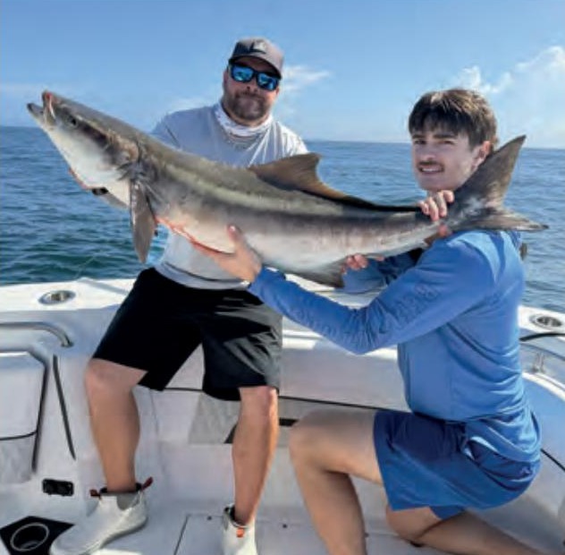 Two anglers holding a big cobia on the deck of a boat