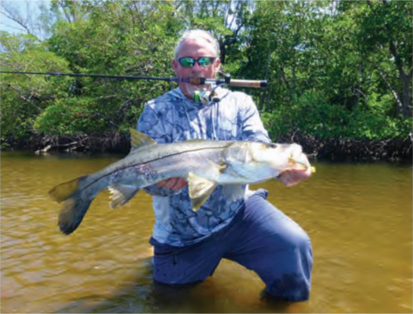An angler kneeling in shallow water with a big snook